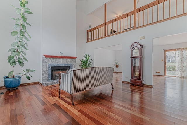 living room with wood-type flooring, a towering ceiling, and a tiled fireplace