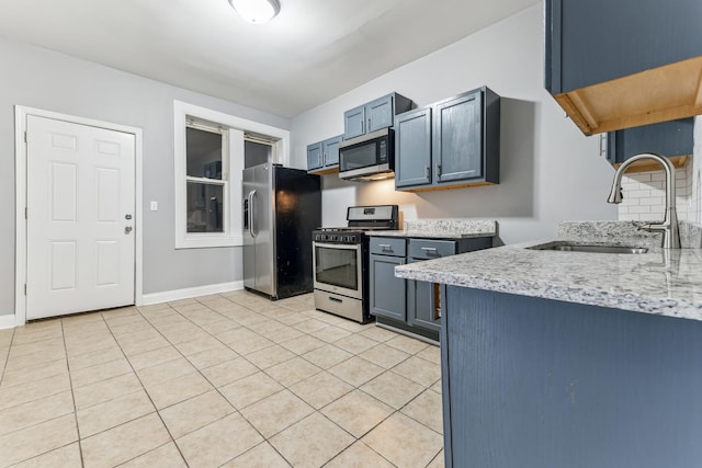 kitchen featuring sink, light stone countertops, blue cabinetry, light tile patterned flooring, and stainless steel appliances