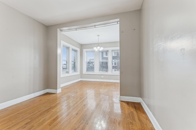 empty room featuring wood-type flooring and a notable chandelier