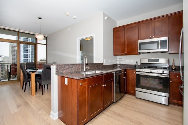 kitchen with stainless steel appliances, light hardwood / wood-style flooring, dark stone countertops, and sink