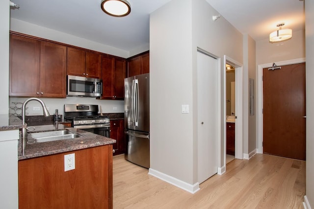 kitchen with dark stone countertops, light wood-type flooring, sink, and appliances with stainless steel finishes