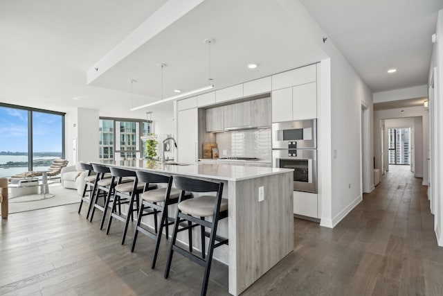 kitchen with a kitchen bar, a kitchen island with sink, sink, pendant lighting, and a water view