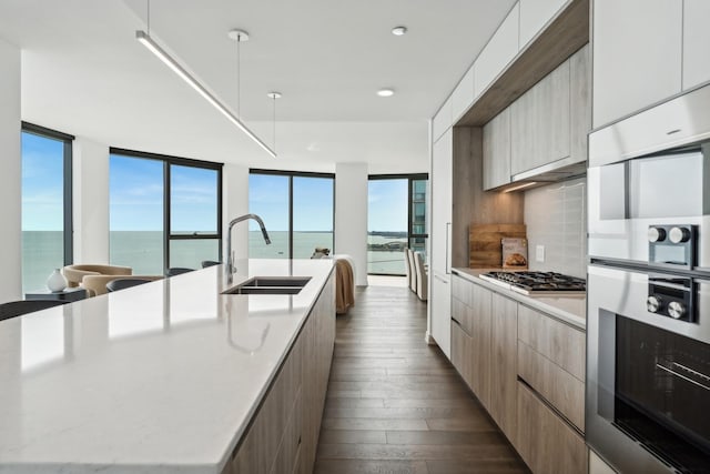 kitchen featuring backsplash, stainless steel gas cooktop, a spacious island, sink, and a water view