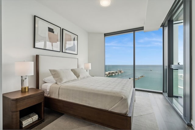 bedroom featuring access to outside, a water view, wood-type flooring, and a wall of windows