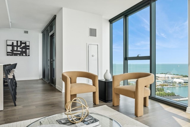 living area with a wealth of natural light, a water view, wood-type flooring, and a wall of windows