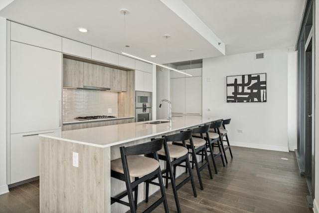 kitchen with a breakfast bar, a center island with sink, dark hardwood / wood-style floors, and stainless steel gas cooktop