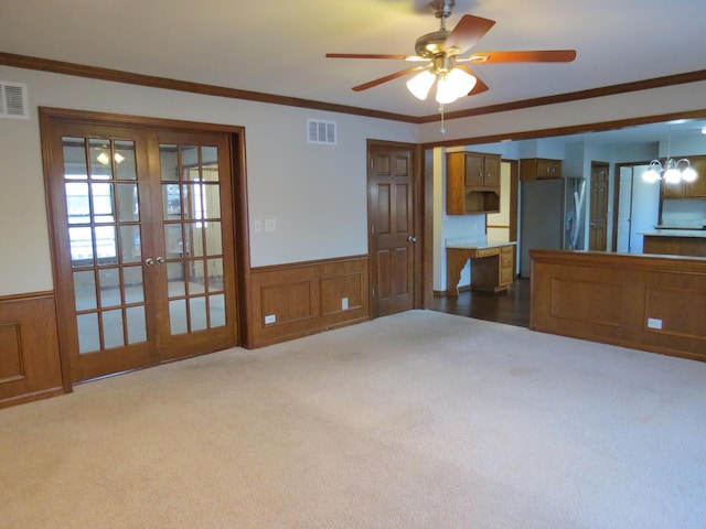 unfurnished living room with french doors, carpet, ceiling fan with notable chandelier, and ornamental molding