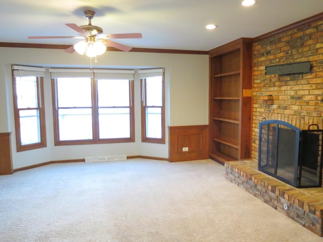 unfurnished living room with a fireplace, light colored carpet, ceiling fan, and crown molding