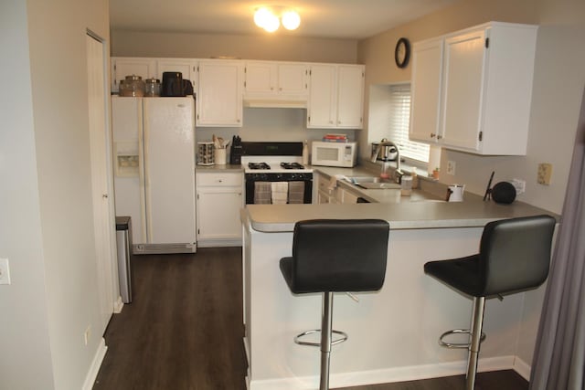 kitchen with white cabinetry, sink, kitchen peninsula, white appliances, and a breakfast bar