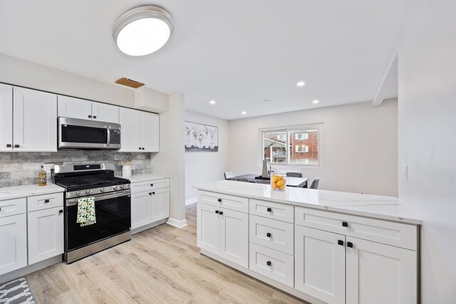 kitchen featuring decorative backsplash, appliances with stainless steel finishes, light stone counters, white cabinets, and light hardwood / wood-style floors