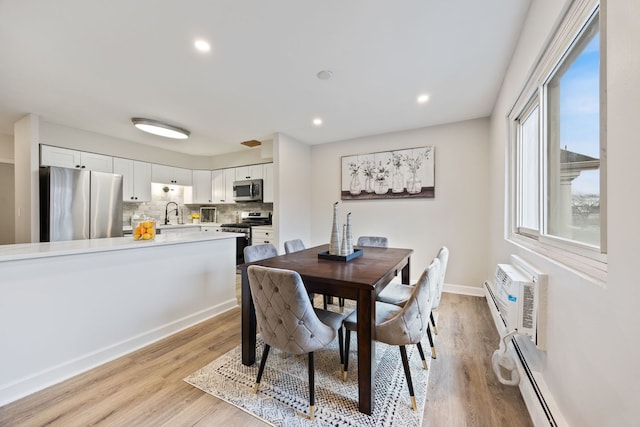 dining room featuring a baseboard radiator, a wall unit AC, light hardwood / wood-style floors, and sink