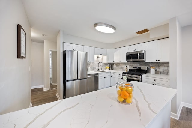 kitchen with light stone countertops, appliances with stainless steel finishes, tasteful backsplash, white cabinets, and dark hardwood / wood-style floors