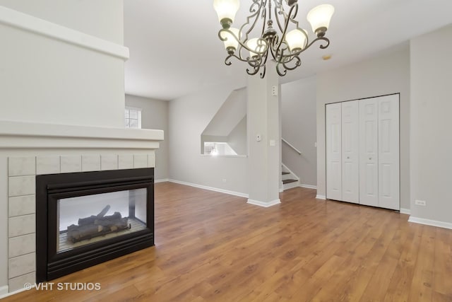 unfurnished living room with hardwood / wood-style floors, a tile fireplace, and an inviting chandelier