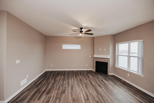 unfurnished living room with ceiling fan, dark wood-type flooring, and a tiled fireplace