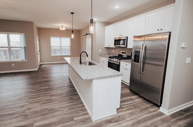 kitchen with stainless steel appliances, a kitchen island with sink, sink, a barn door, and white cabinetry