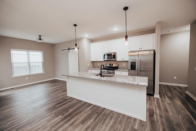 kitchen featuring a center island with sink, sink, a barn door, appliances with stainless steel finishes, and white cabinetry