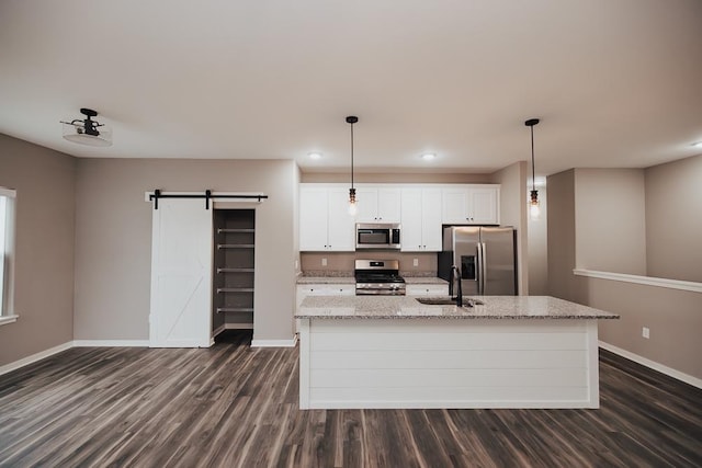 kitchen with appliances with stainless steel finishes, a barn door, a center island with sink, and white cabinetry