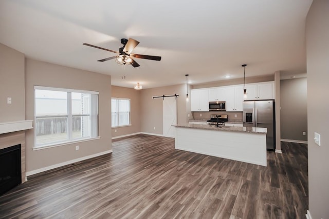 kitchen with ceiling fan, a barn door, light stone counters, white cabinets, and appliances with stainless steel finishes