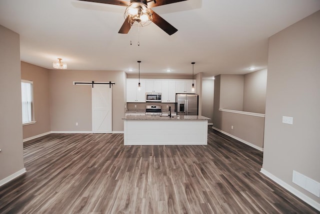 kitchen with white cabinetry, stainless steel appliances, a barn door, light stone counters, and pendant lighting