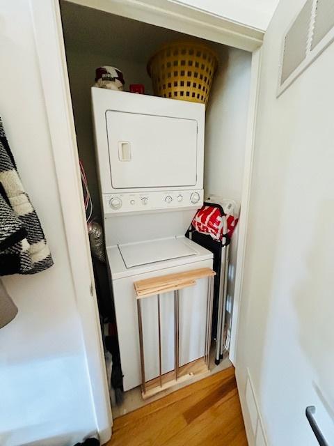 laundry room with light hardwood / wood-style floors and stacked washer and dryer