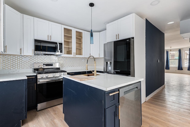 kitchen with decorative light fixtures, glass insert cabinets, appliances with stainless steel finishes, and light wood finished floors