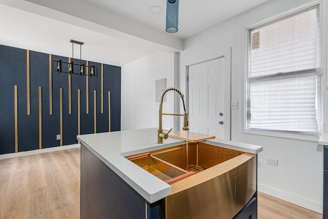 kitchen featuring decorative light fixtures, light wood-style flooring, an island with sink, and baseboards