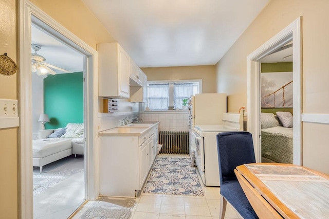 kitchen featuring radiator, ceiling fan, sink, stove, and white cabinets