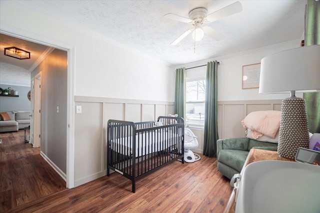 bedroom with ceiling fan, dark hardwood / wood-style flooring, a textured ceiling, a crib, and ornamental molding