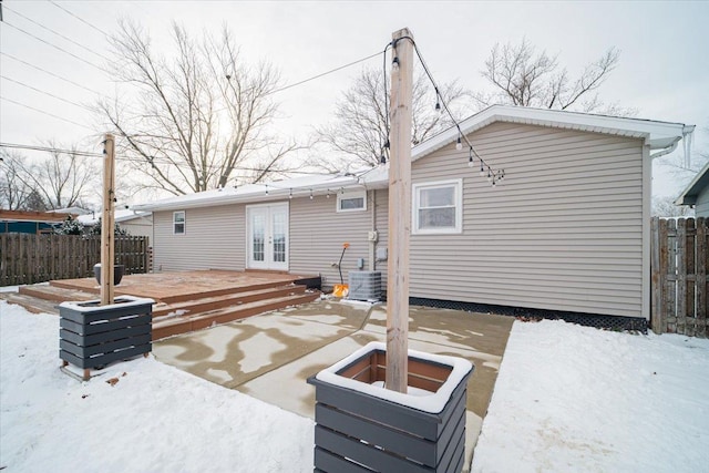 snow covered house with french doors, a deck, and central air condition unit