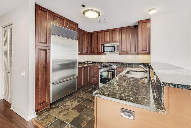 kitchen featuring kitchen peninsula, sink, dark stone countertops, and appliances with stainless steel finishes