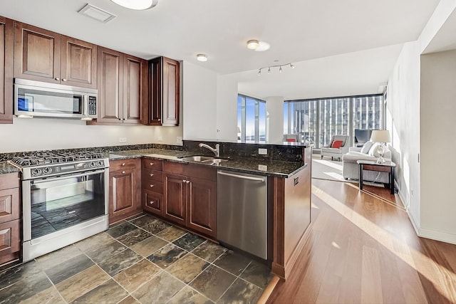 kitchen with dark stone countertops, kitchen peninsula, sink, and appliances with stainless steel finishes