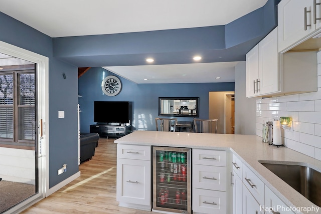 kitchen with wine cooler, light hardwood / wood-style floors, kitchen peninsula, white cabinetry, and backsplash