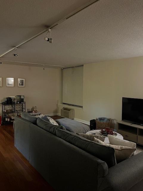 living room with track lighting, a textured ceiling, hardwood / wood-style flooring, and a wall mounted AC