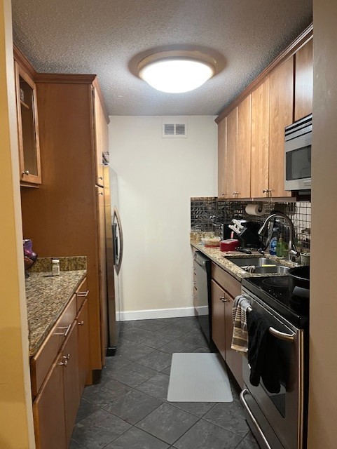 kitchen featuring sink, a textured ceiling, light stone counters, and appliances with stainless steel finishes