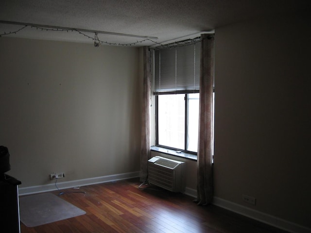 spare room featuring a textured ceiling, dark hardwood / wood-style flooring, and an AC wall unit