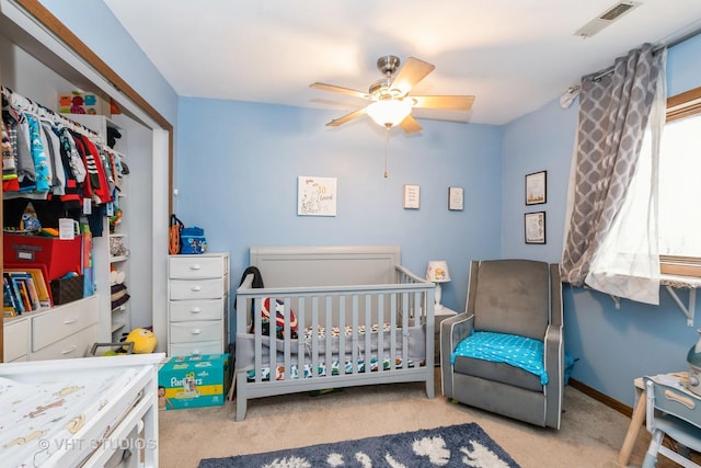 bedroom with a nursery area, light colored carpet, ceiling fan, and a closet