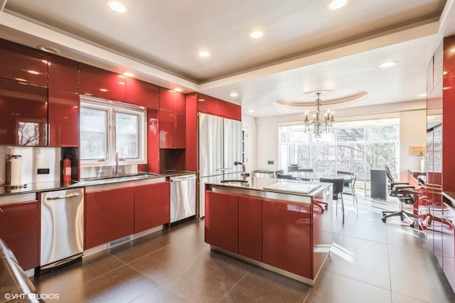 kitchen with stainless steel dishwasher, a raised ceiling, sink, a notable chandelier, and an island with sink