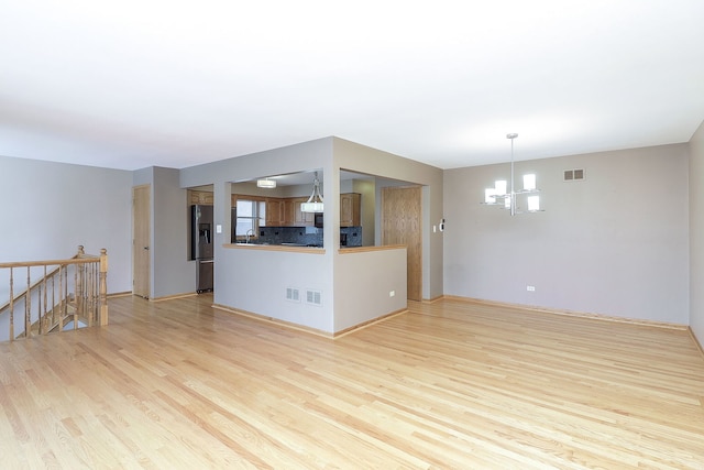 unfurnished living room with a notable chandelier and light wood-type flooring