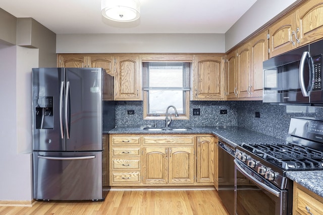 kitchen with sink, backsplash, dark stone counters, light hardwood / wood-style floors, and stainless steel appliances