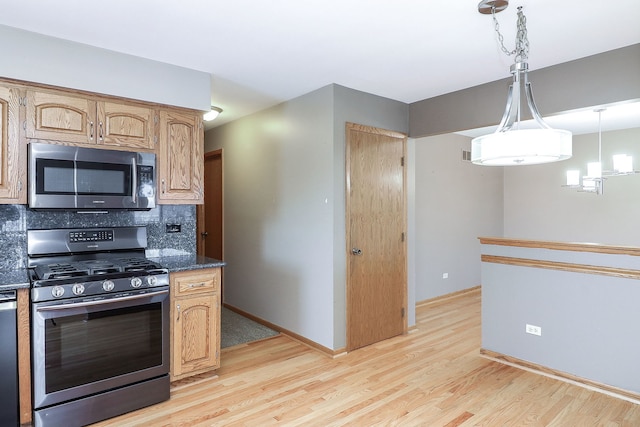 kitchen featuring dark stone counters, hanging light fixtures, decorative backsplash, stainless steel appliances, and light wood-type flooring