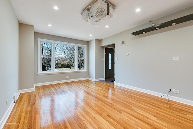 empty room featuring a notable chandelier and light wood-type flooring