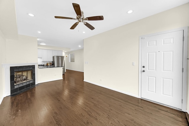 unfurnished living room featuring a tiled fireplace, ceiling fan, and dark hardwood / wood-style flooring