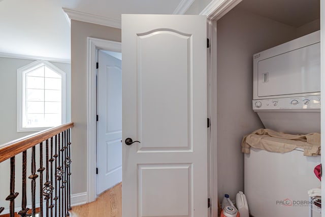 laundry area with light wood-type flooring, ornamental molding, and stacked washer / dryer