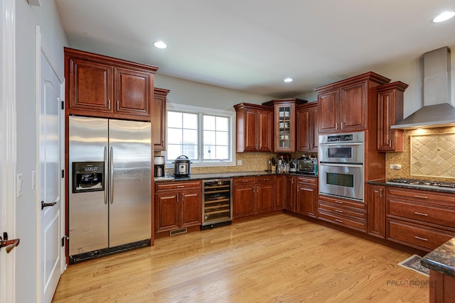 kitchen with backsplash, wall chimney range hood, wine cooler, light wood-type flooring, and stainless steel appliances