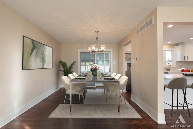 dining space with sink, dark hardwood / wood-style floors, and an inviting chandelier