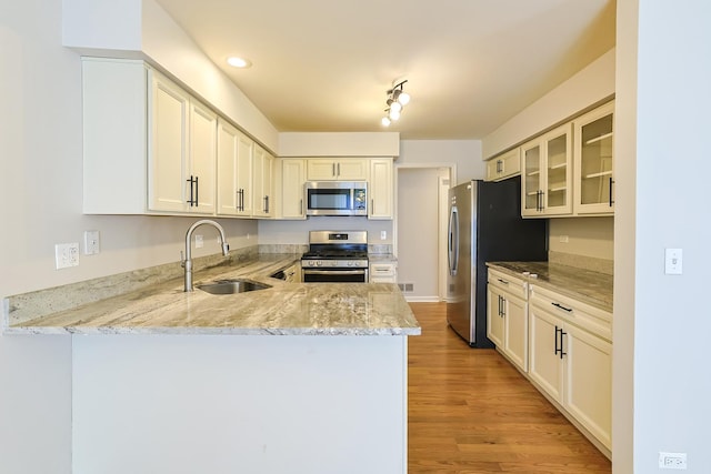 kitchen with sink, light wood-type flooring, light stone counters, kitchen peninsula, and stainless steel appliances