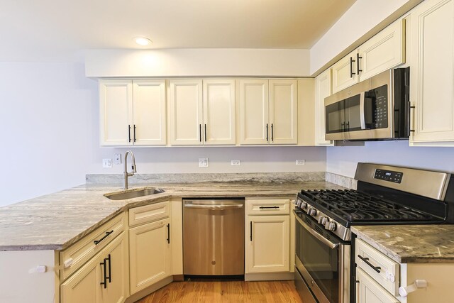 kitchen featuring light stone countertops, stainless steel appliances, kitchen peninsula, and sink