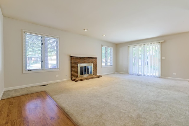 unfurnished living room featuring a healthy amount of sunlight, light colored carpet, and a brick fireplace