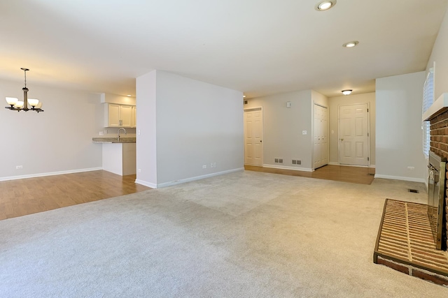 unfurnished living room featuring a notable chandelier, sink, light carpet, and a brick fireplace