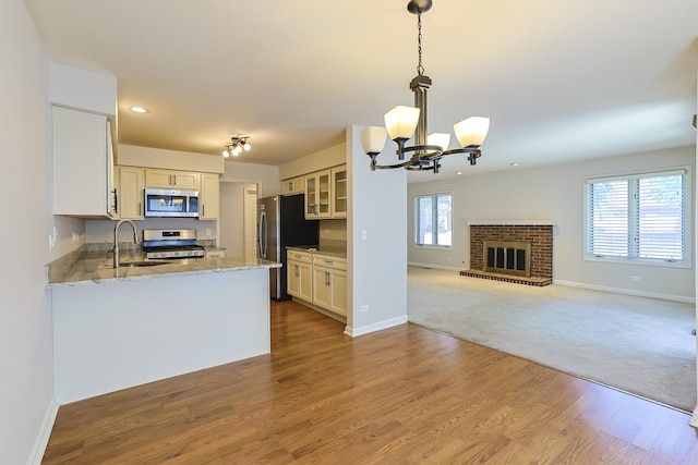 kitchen with sink, a brick fireplace, white cabinetry, stainless steel appliances, and a chandelier